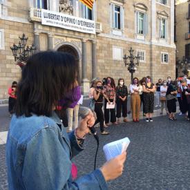 Una dona d'esquenes parlant amb un micròfon i gent concentrada a la plaça