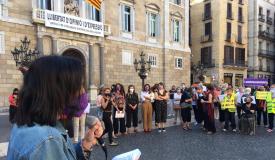 Una dona d'esquenes parlant amb un micròfon i gent concentrada a la plaça